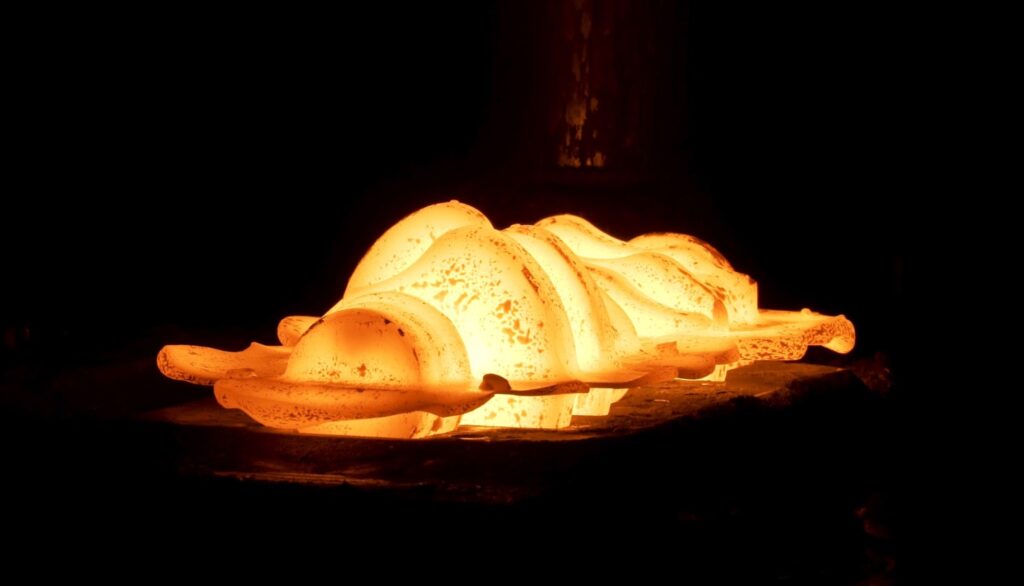 Hot metal billets glowing inside a forging press during a high-temperature metalforming process.